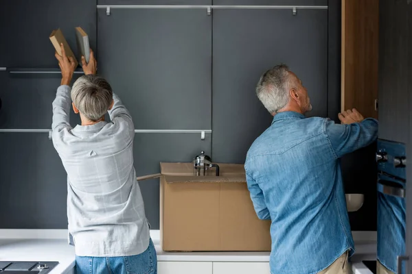 Vue arrière de l'homme mature ouvrant la porte et la femme arrangeant des livres dans la maison neuve — Photo de stock