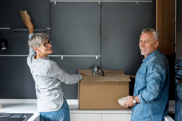 Uomo maturo e donna sorridente disimballaggio scatola in nuova casa — Foto stock