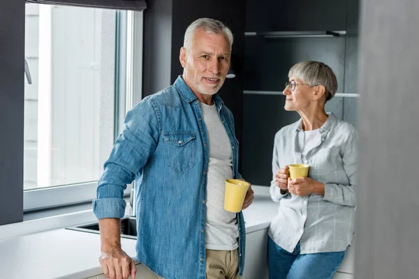 Uomo sorridente e donna matura che tiene le tazze in una nuova casa — Foto stock