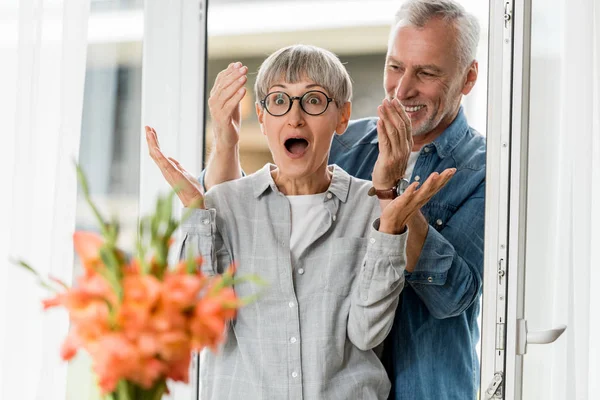 Selective focus of smiling man and shocked woman looking at bouquet in new house — Stock Photo