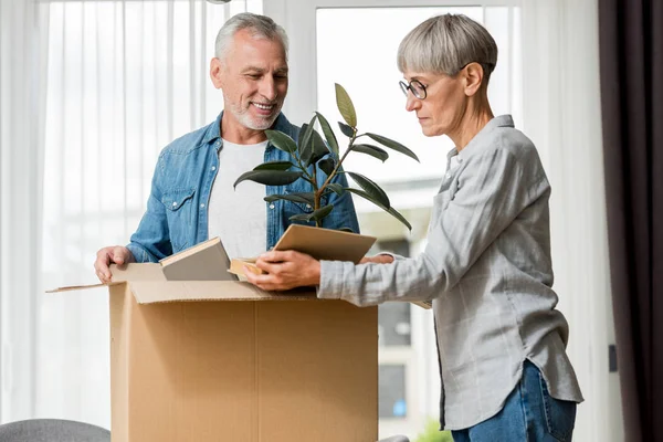 Hombre sonriente y mujer madura desembalaje caja en casa nueva - foto de stock