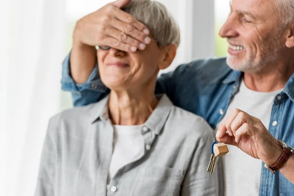 Enfoque selectivo del hombre sonriente sosteniendo las llaves de la nueva casa y oscureciendo la cara de la mujer - foto de stock