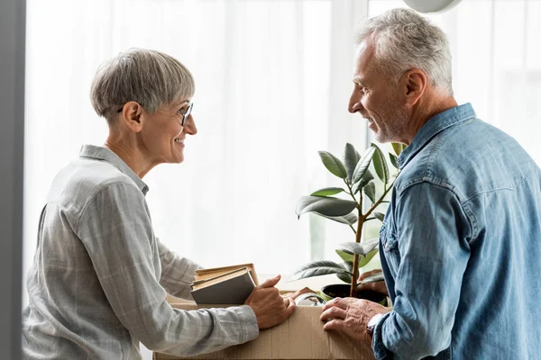 Vue latérale de l'homme souriant et de la femme mûre déballer la boîte dans une nouvelle maison — Photo de stock