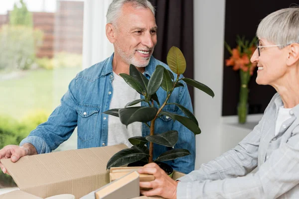 Lächelnder Mann und reife Frau beim Auspacken der Schachtel im neuen Haus — Stockfoto