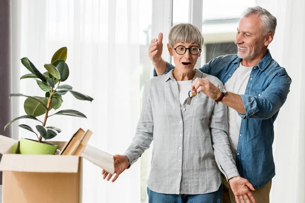 Homme souriant tenant les clés de la nouvelle maison et regardant femme surprise — Photo de stock