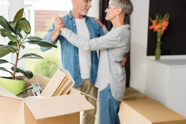 Selective focus of box with plant and books and mature couple in new house on background — Stock Photo