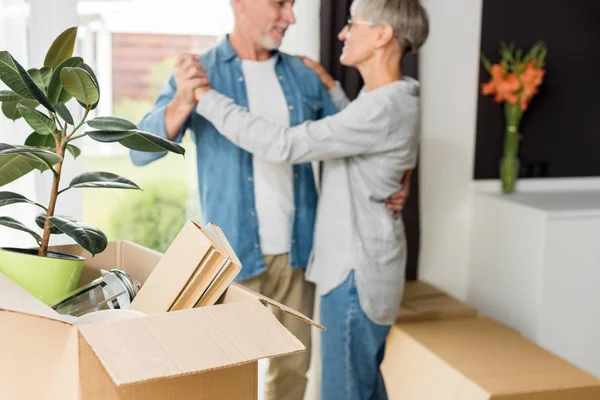 Selektiver Fokus der Schachtel mit Pflanzen und Büchern und reifes Paar im neuen Haus im Hintergrund — Stockfoto