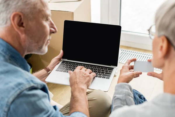 Cropped view of mature man with laptop and woman holding empty card in new house — Stock Photo