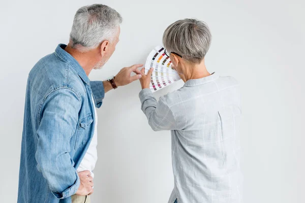 Back view of mature man pointing with finger at palette and woman holding it in new house — Stock Photo