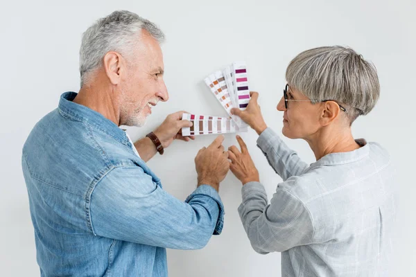 Mature man and woman pointing with fingers at palette in new house — Stock Photo