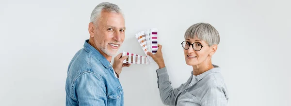 Panoramaaufnahme eines reifen Mannes und einer reifen Frau mit Palette, die in einem neuen Haus in die Kamera schauen — Stockfoto