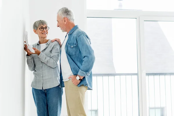 Lächelnder Mann schaut reife Frau mit Palette in neuem Haus an — Stockfoto