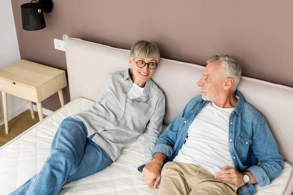 Reifer Mann und lächelnde Frau Händchen haltend im Bett in neuem Haus — Stockfoto