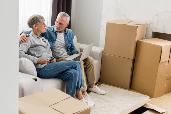 Mature man with laptop hugging woman in new house — Stock Photo