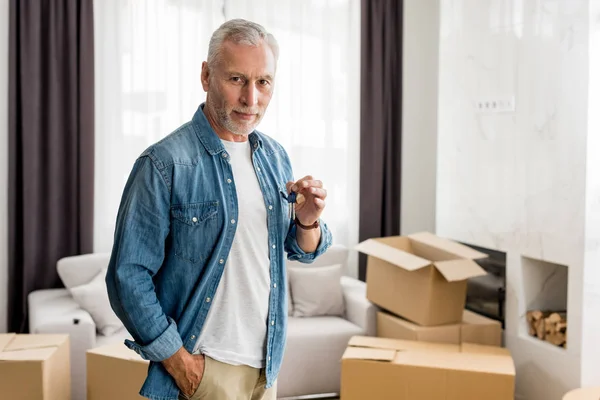 Mature man holding keys and looking at camera in new house — Stock Photo