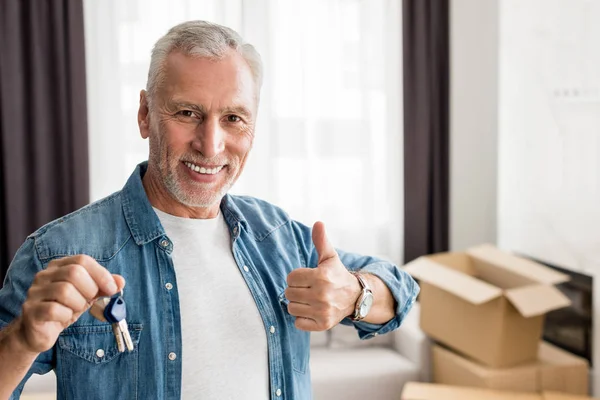 Smiling man holding keys and showing like in new house — Stock Photo