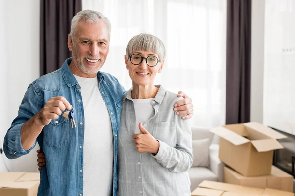 Sonriente hombre sosteniendo llaves y mujer mostrando como en casa nueva - foto de stock