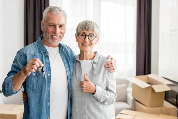 Uomo sorridente che tiene le chiavi e la donna che mostra come in nuova casa — Foto stock