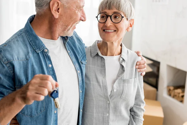 Vista recortada de hombre sonriente sosteniendo las llaves y mirando a la mujer en la nueva casa - foto de stock