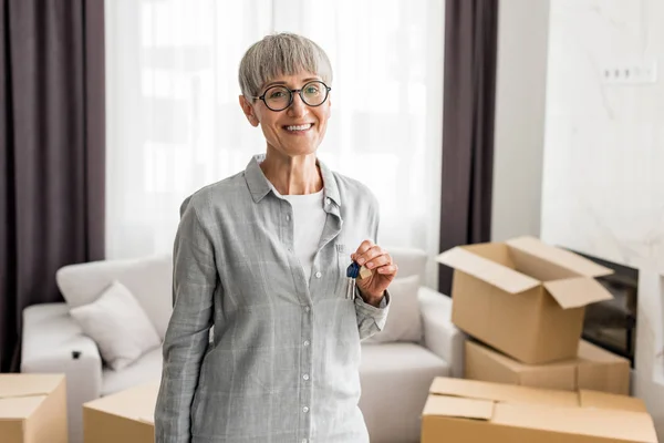 Smiling woman holding keys and looking at camera in new house — Stock Photo
