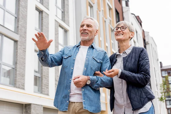 Vista basso angolo di uomo maturo e donna sorridente guardando lontano vicino a nuovi edifici — Foto stock