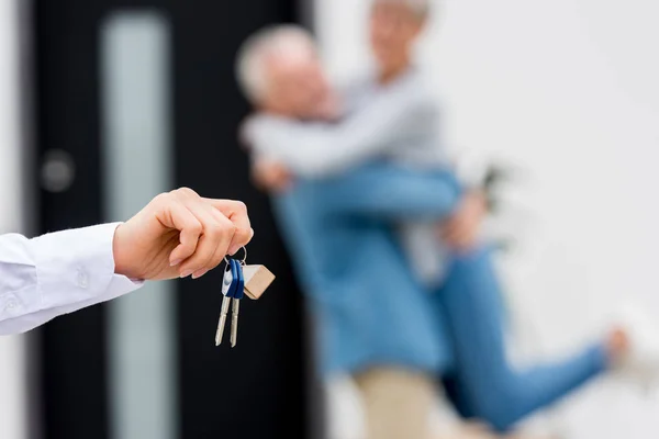 Foyer sélectif du courtier détenant les clés de la maison neuve et le couple sur fond — Photo de stock