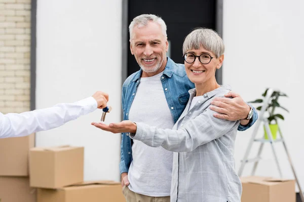 Cropped view of broker giving keys of new house to smiling man and woman — Stock Photo