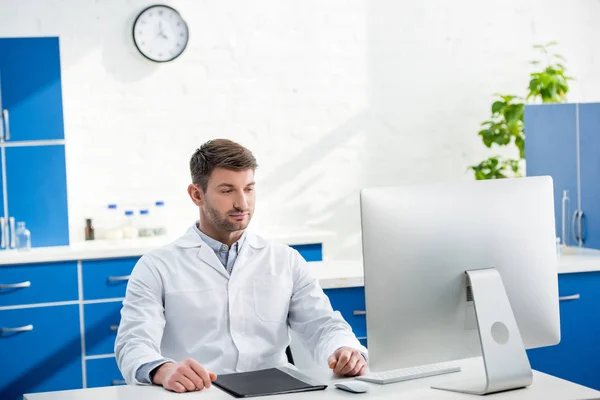 Nutritionniste moléculaire assis à table et regardant l'ordinateur en laboratoire — Photo de stock