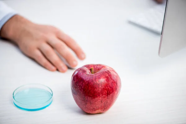 Selective focus of ripe and fresh apple on table and molecular nutritionist on background — Stock Photo