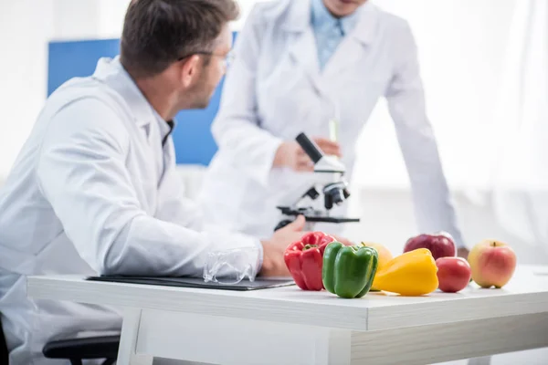 Selective focus of bell peppers, apples, tomato and molecular nutritionists on background — Stock Photo