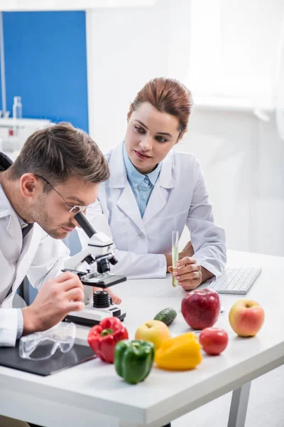 Nutritionniste moléculaire utilisant un microscope et son collègue tenant une éprouvette — Photo de stock