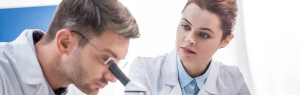 Prise de vue panoramique du nutritionniste moléculaire regardant son collègue au microscope — Photo de stock