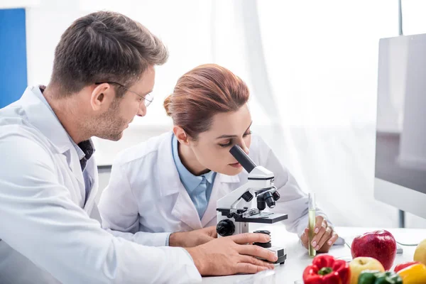 Nutricionista molecular usando microscópio e colega olhando para ela — Fotografia de Stock