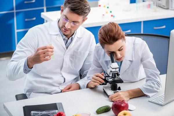 Molecular nutritionist using microscope and colleague holding test tube — Stock Photo