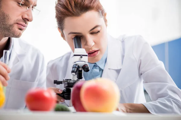 Selective focus of molecular nutritionist using microscope and colleague holding test tube — Stock Photo