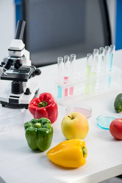 Microscopio, frutas, verduras, tubos de ensayo en la mesa en el laboratorio - foto de stock