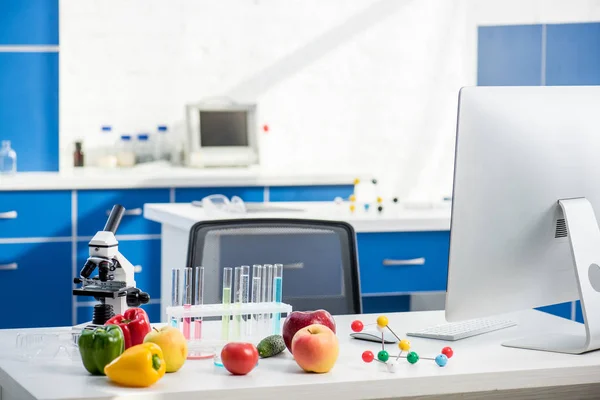 Microscópio, frutas, legumes, tubos de ensaio e computador na mesa em laboratório — Fotografia de Stock