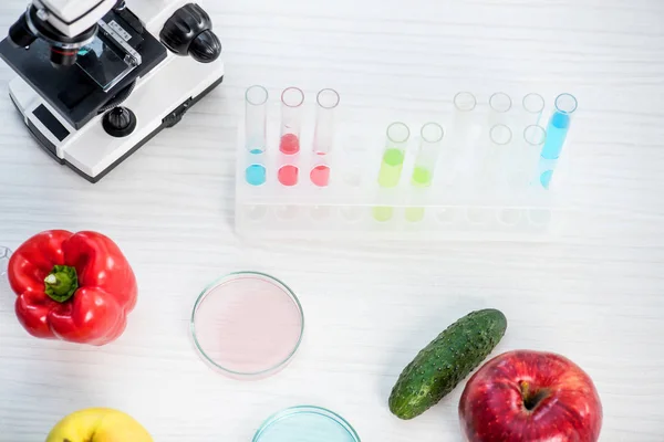Високий кут зору на мікроскоп, фрукти, овочі, пробірки та посуд Петрі на столі в лабораторії — стокове фото