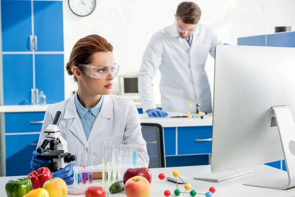 Enfoque selectivo de nutricionista molecular mirando a la computadora y colega en el fondo - foto de stock