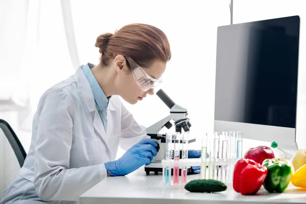 Visão lateral do nutricionista molecular usando microscópio e sentado à mesa — Fotografia de Stock