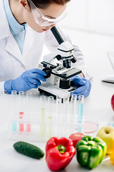 Ausgeschnittene Ansicht eines molekularen Ernährungswissenschaftlers unter dem Mikroskop und am Tisch sitzend — Stockfoto