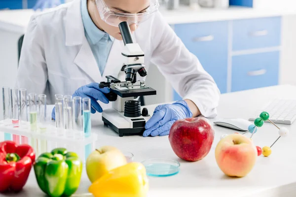 Vista cortada de nutricionista molecular usando microscópio e sentado à mesa — Fotografia de Stock