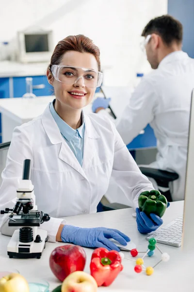 Nutricionista molecular sonriente sosteniendo pimiento y mirando a la cámara - foto de stock