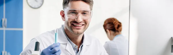 Panoramic shot of smiling molecular nutritionist holding test tube — Stock Photo