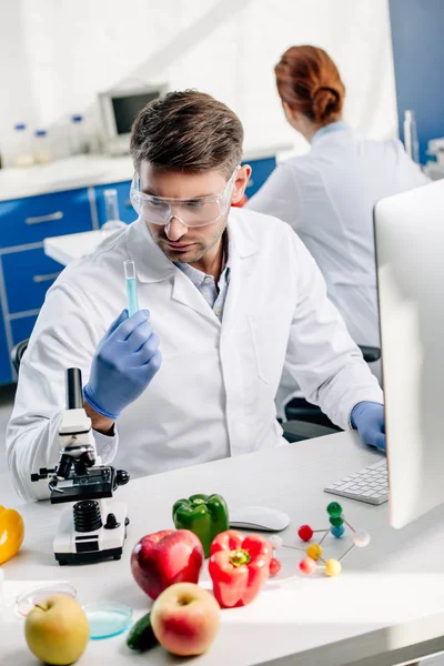 Molecular nutritionist in goggles looking at test tube in lab — Stock Photo