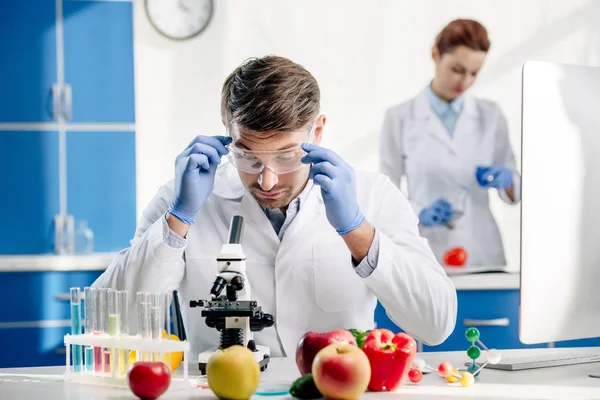 Molecular nutritionist in goggles looking at microscope in lab — Stock Photo