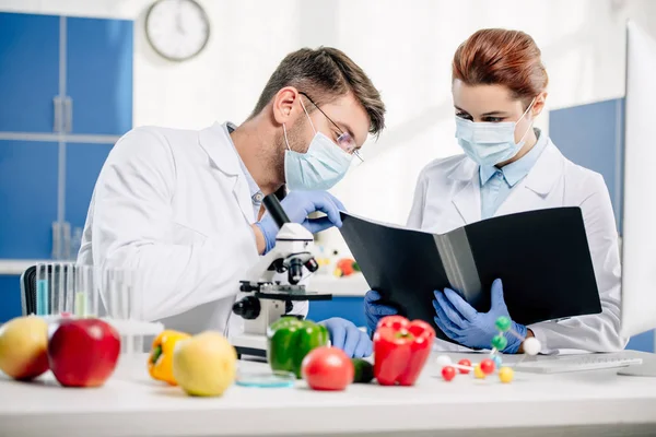 Selective focus of molecular nutritionists in medical masks looking at folder — Stock Photo