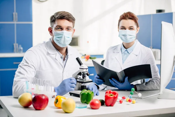 Molecular nutritionists in medical masks looking at camera in lab — Stock Photo