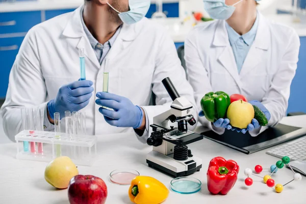 Vista recortada de nutricionistas moleculares sosteniendo tubos de ensayo y alimentos - foto de stock