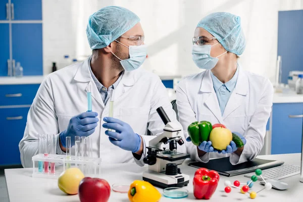 Molecular nutritionists holding test tubes, fruit and vegetables — Stock Photo